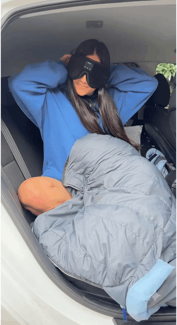 Person lying in a sleeping bag inside a vehicle with a blue jacket on wearing Dreamy Sounds Sleep Mask | Bluetooth Sleep Mask