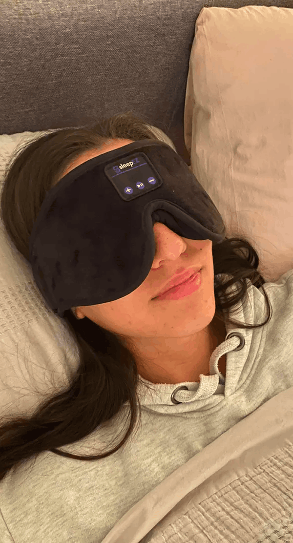 A woman lying in bed wearing Dreamy Sounds Sleep Mask | Bluetooth Sleep Mask with a built-in digital temperature control panel on the forehead.