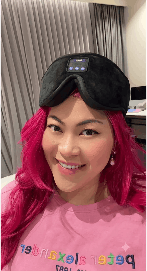 A woman with bright pink hair wearing Dreamy Sounds Sleep Mask | Bluetooth Sleep Mask, paired with a pink t-shirt in an indoor setting.